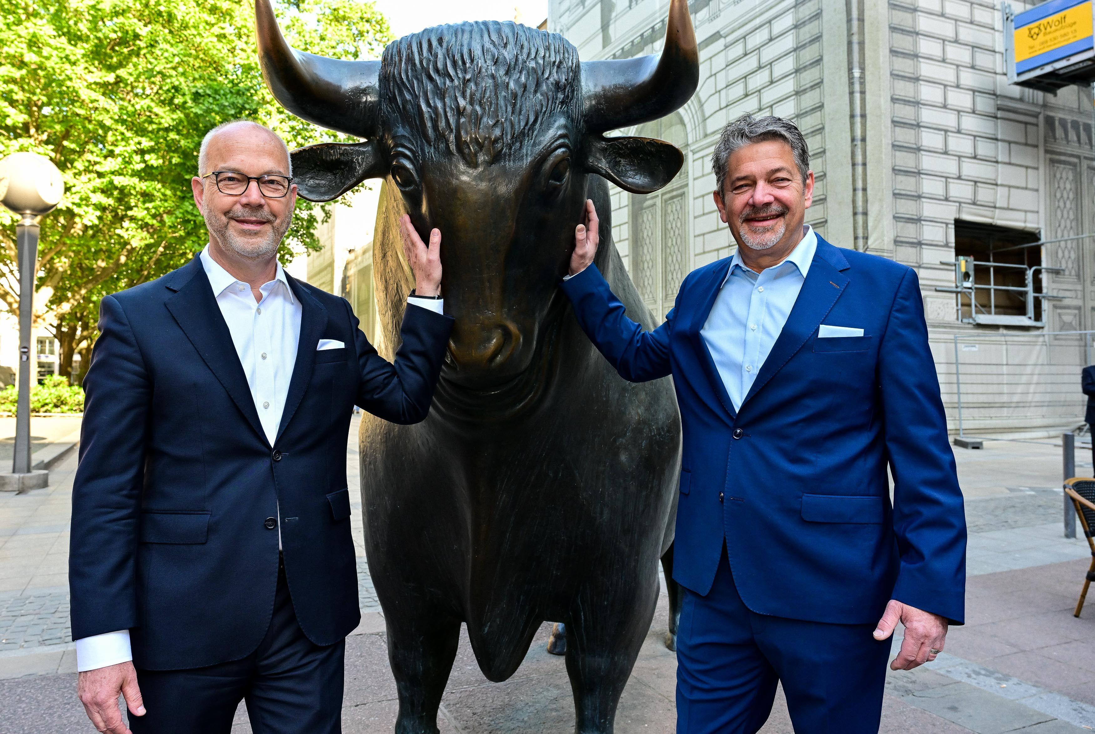 Johannes Linden und Vorstandskollege Dr. Konstantin Kurfiss stehen rechts und links der Bullen-Skulptur vor der Frankfurter Börse.