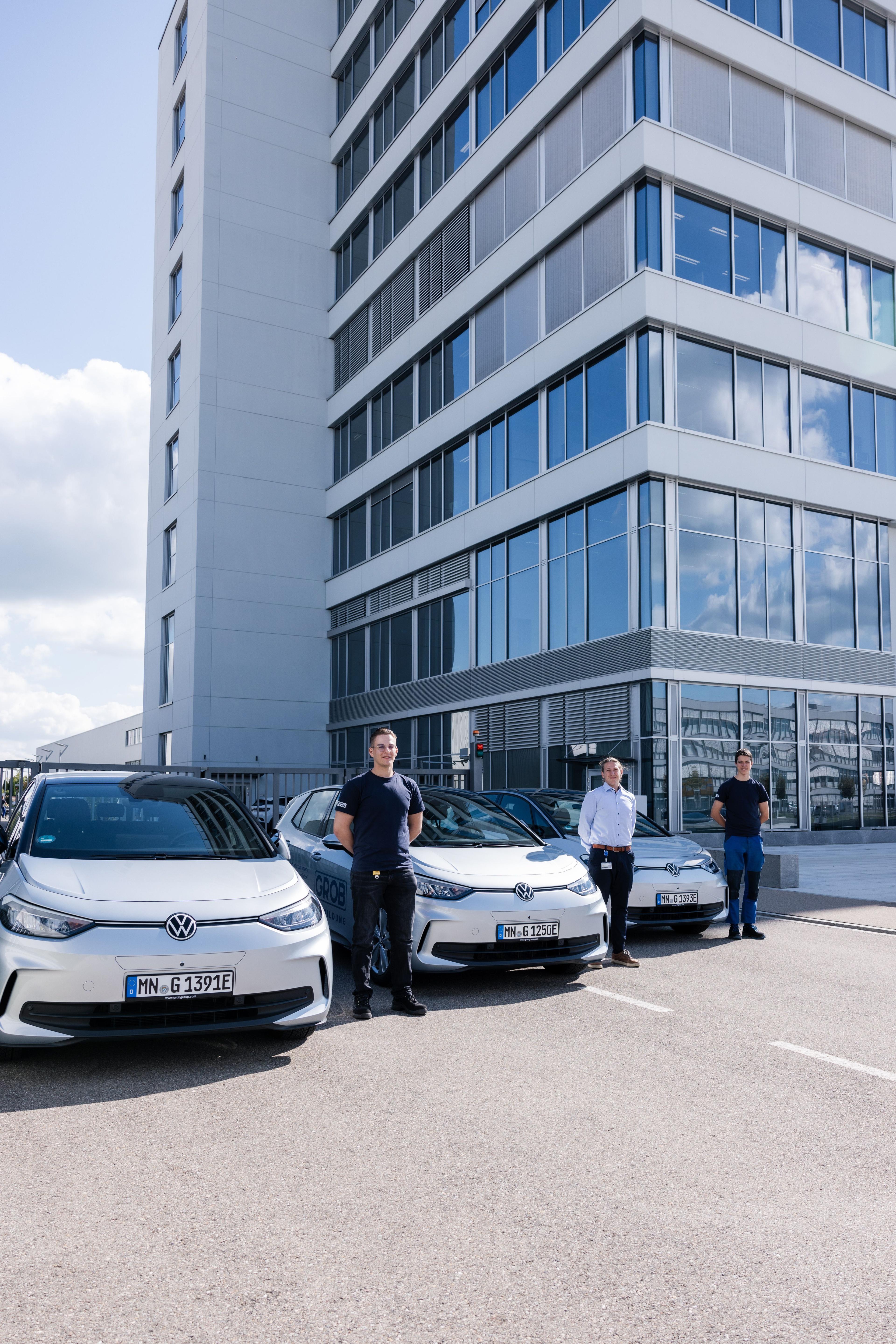 Drei junge Männer stehen neben den drei E-Azubimobile-Autos.