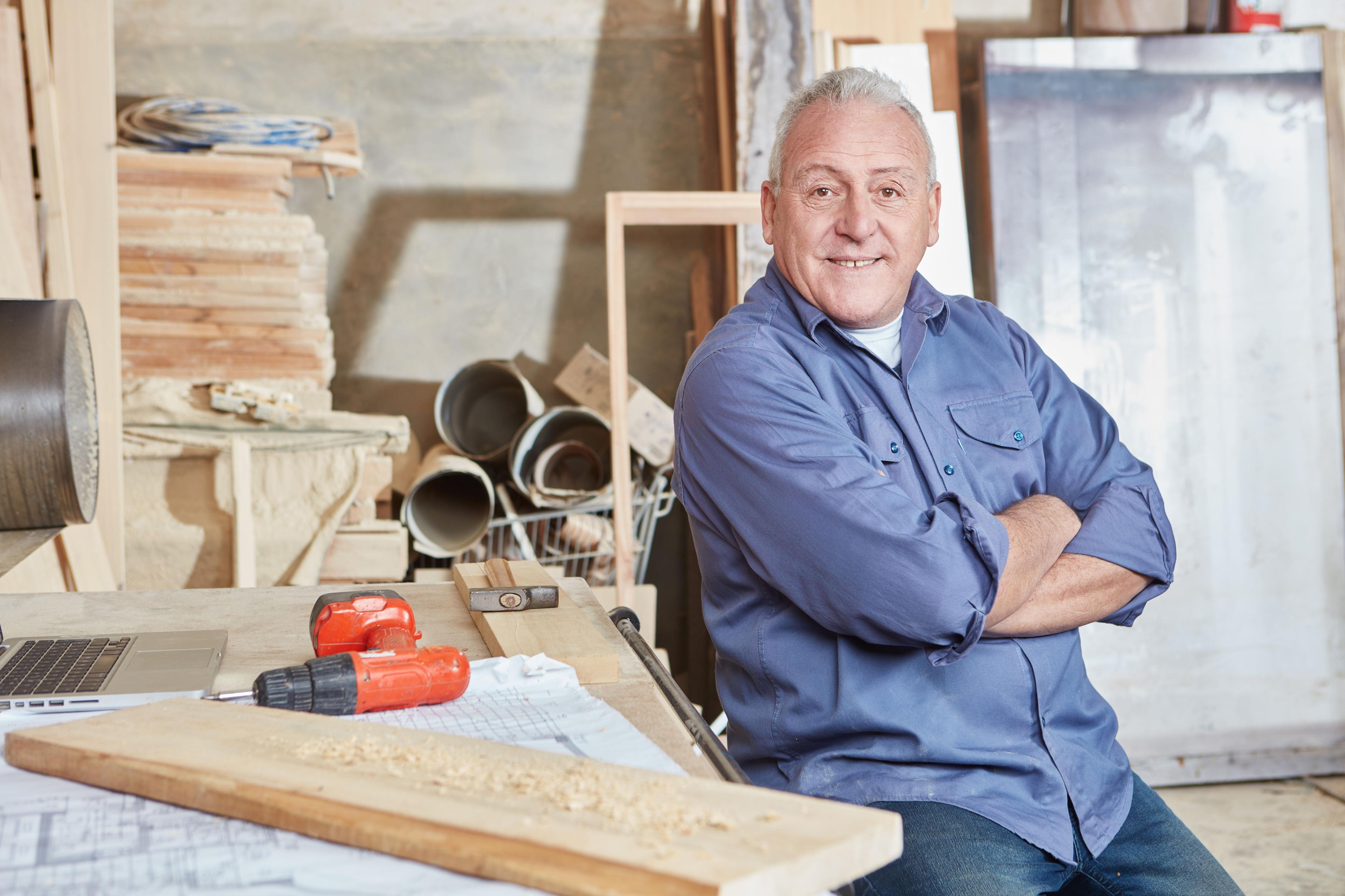 Älterer Arbeitnehmer sitzt auf einer Werkbank.