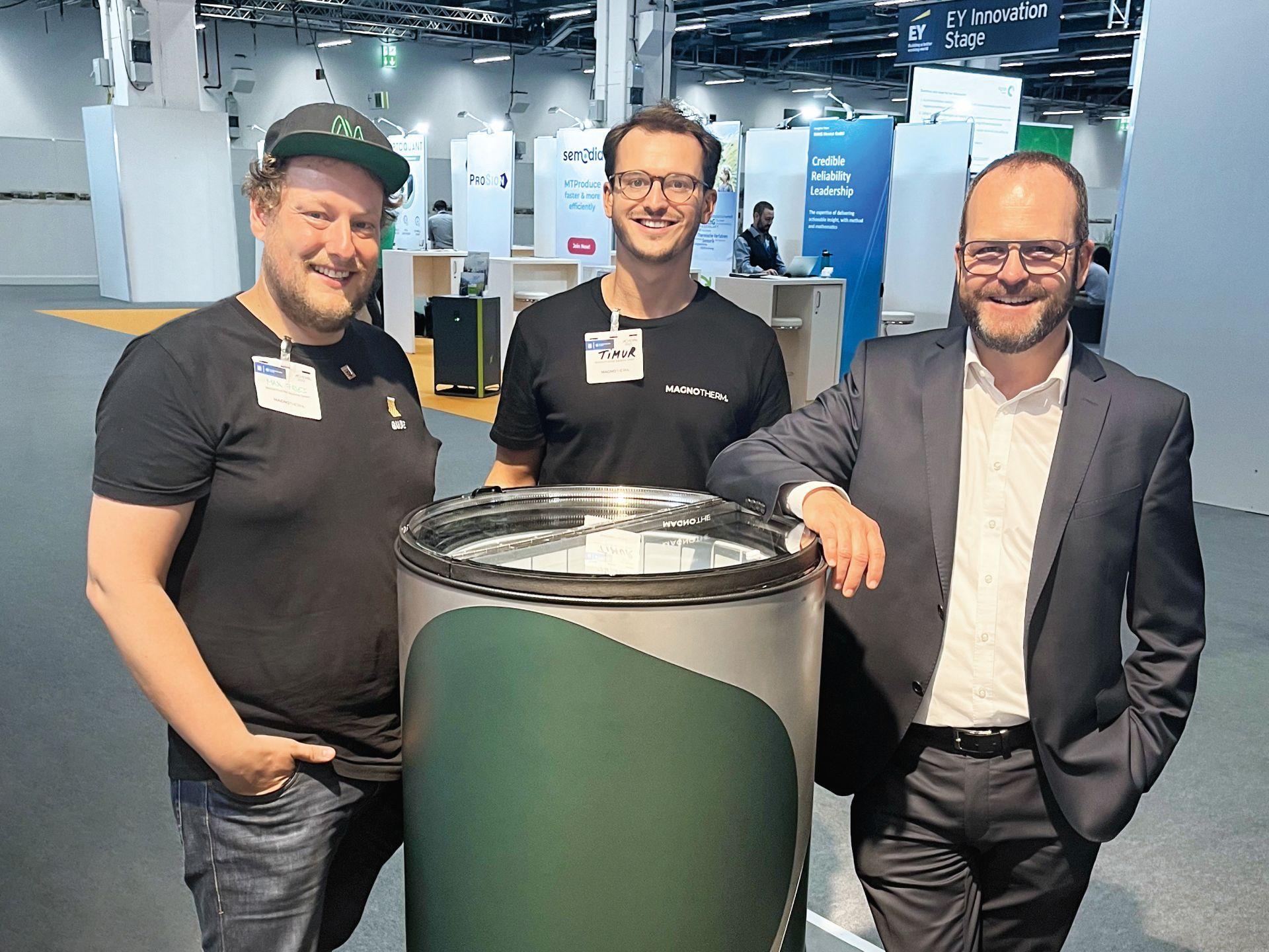 Die im Bildtext genannten Personen stehen in einem Messe-Umfeld beieinander.