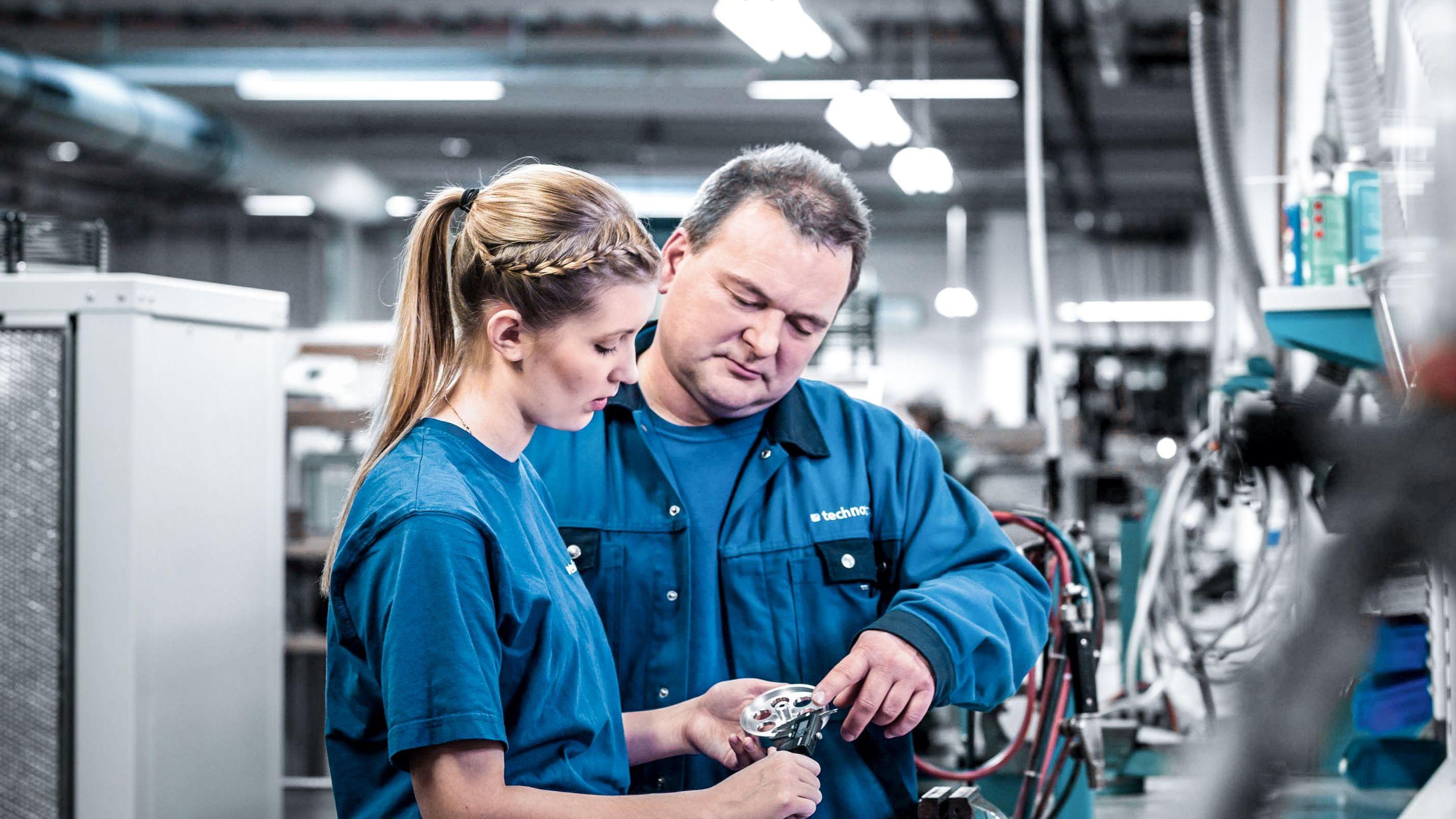 Ein Mentor erklärt einer Auszubildenden etwas in der Produktion.