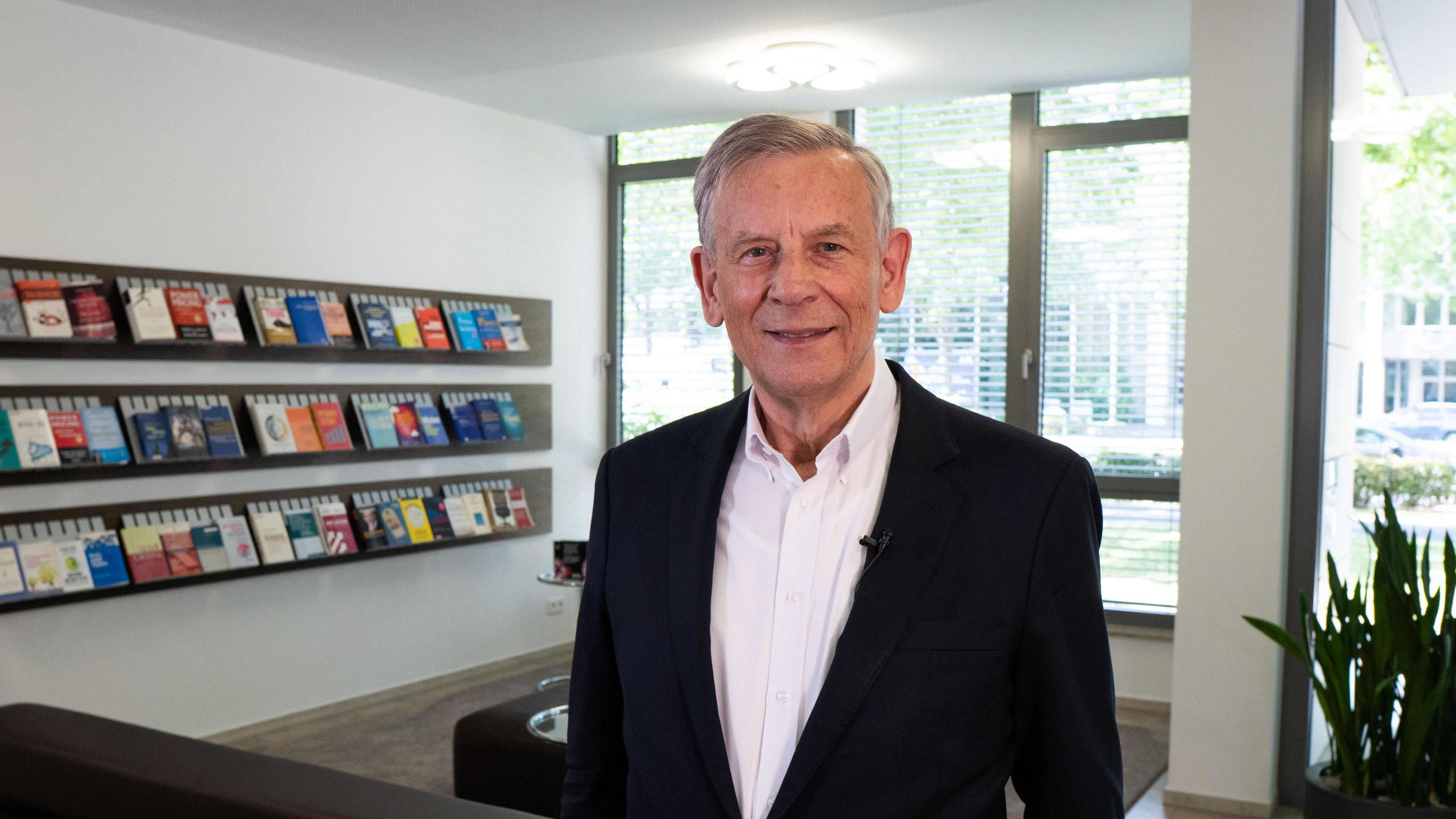 Prof. Dr. Dr. h.c. mult. Hermann Simon steht vor einer Bücherwand in der Lobby von Simon-Kucher in Bonn.