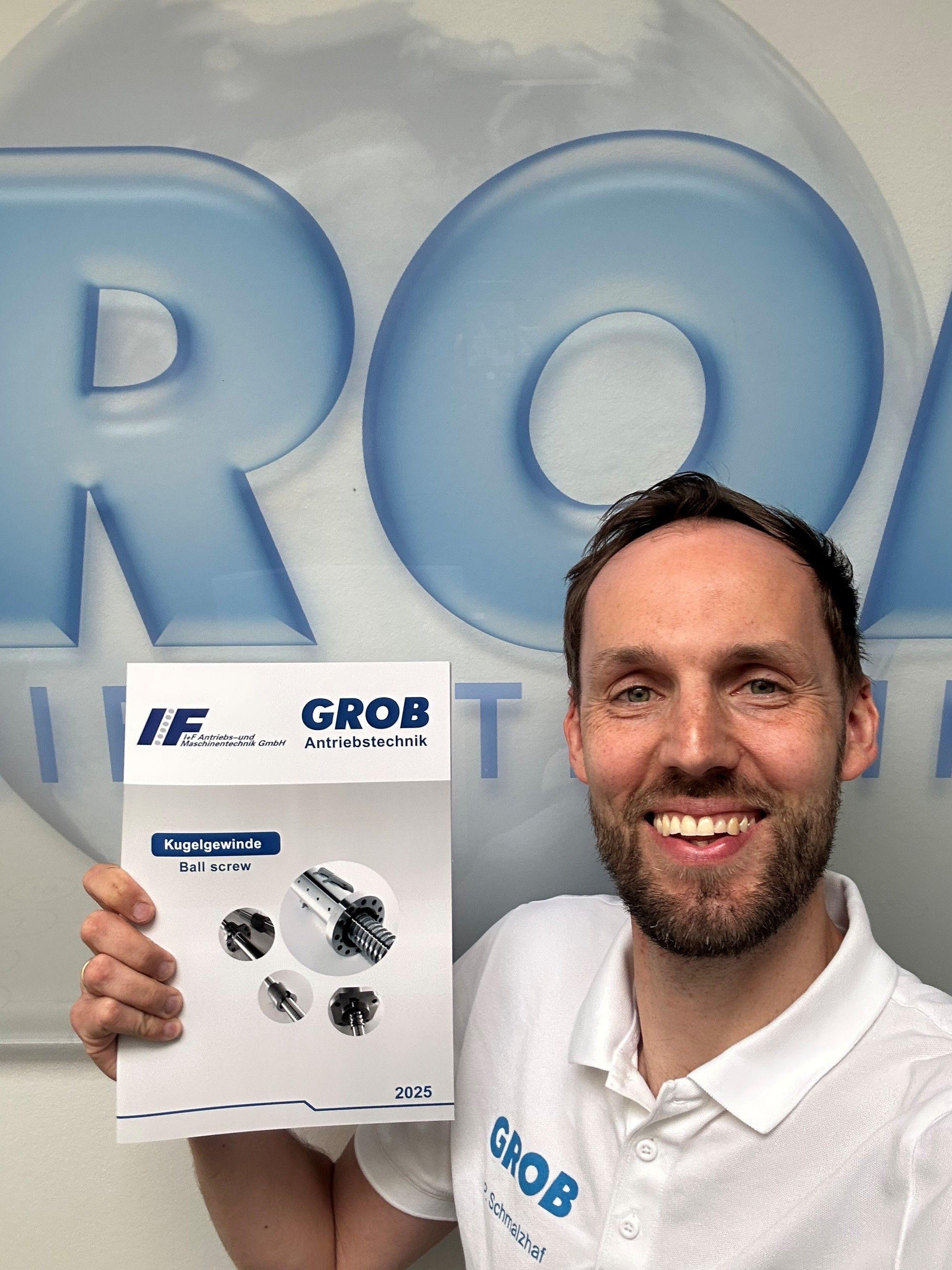 Philipp Schmalzhaf zeigt lachend einen Prospekt mit Kugelgewinden von Grob Antriebstechnik.